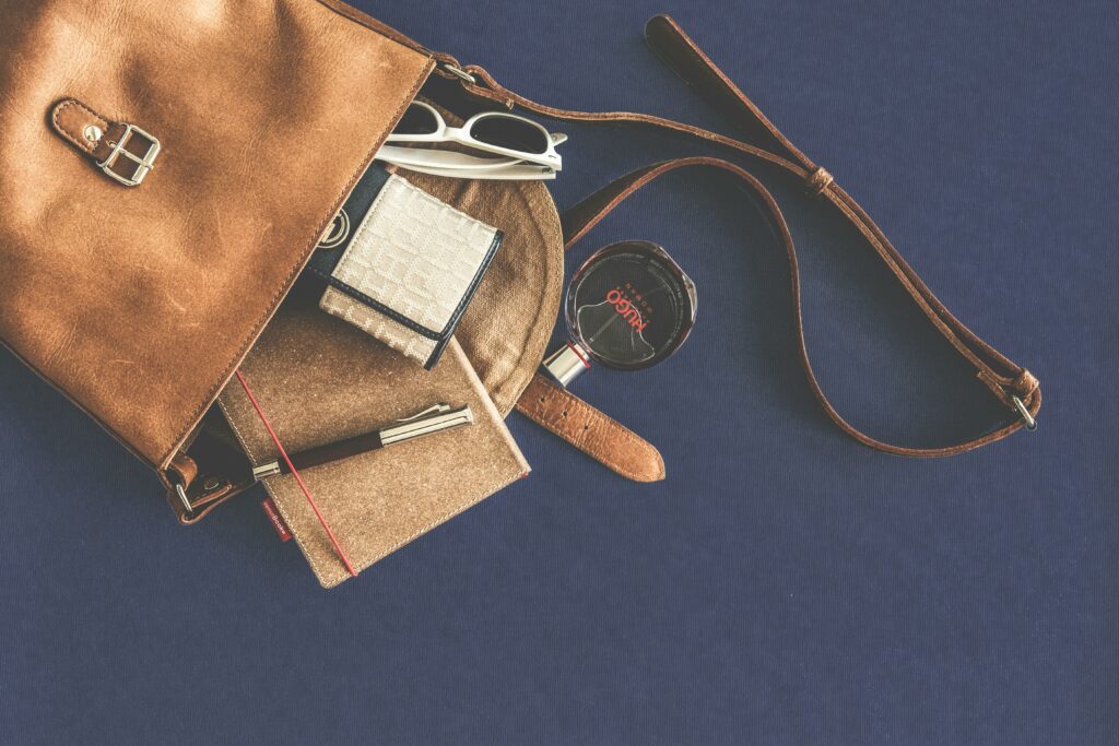 Stylish flat lay of a leather handbag with luxury accessories including sunglasses, wallet, notebook, and pen.